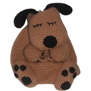 May include: A brown crocheted stuffed dog toy with black ears, eyes, nose, and paws. The dog is sitting with its eyes closed and its paws tucked under its body.