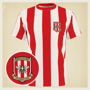 Może przedstawiać: Czerwono-biała koszulka w paski z okrągłym dekoltem i krótkimi rękawami. Koszulka posiada herb Brentford z pszczołą i napisem "BRENTFORD FOUNDED 1889". Koszulka jest w stylu vintage.