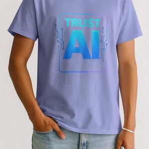 May include: A light purple t-shirt with the text "TRUST AI" in a blue gradient font, framed by a blue and purple circuit board design. The person is wearing light blue jeans.