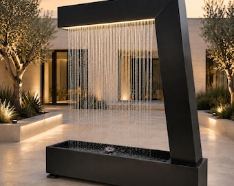 Könnte beinhalten: Ein schwarzer Wasserbrunnen aus Metall für den Außenbereich mit rechteckigem Sockel und L-förmigem Rahmen. Wasser fließt in dünnen, vertikalen Strahlen vom oberen horizontalen Balken in das Becken, beleuchtet durch ein warmes Lichtband.