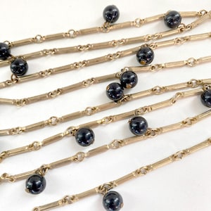 May include: A gold chain necklace with black beads hanging from it. The chain is made of small, linked bars.