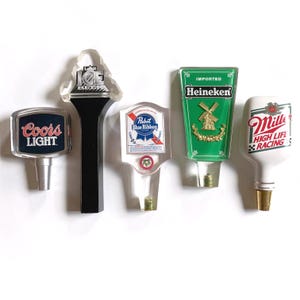 May include: A collection of five beer tap handles. The handles feature logos for Coors Light, Labatt Ice Beer, Pabst Blue Ribbon, Heineken, and Miller High Life. The handles are made of various materials and have different shapes and colors.