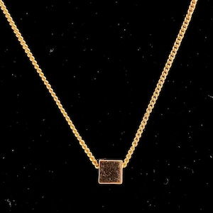 May include: A gold-colored necklace with a square pendant. The chain is a delicate, twisted rope design, and the pendant is a small, solid square. The necklace is displayed against a black background.