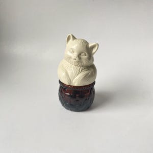 May include: A white ceramic cat figurine sitting inside a brown wicker basket. The cat has a sweet expression and is looking up.
