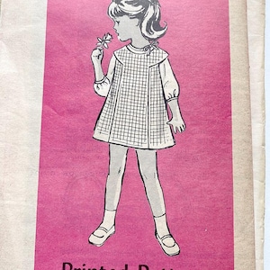 May include: Vintage sewing pattern featuring a line drawing of a young girl in a grid-patterned dress, holding a flower. The illustration is in black and white, set against a pink background. The pattern is for a child's dress.