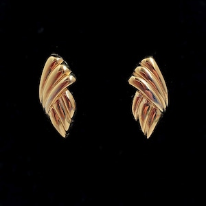 May include: A pair of gold-toned earrings with a geometric design. The earrings are shaped like a wing or a leaf.