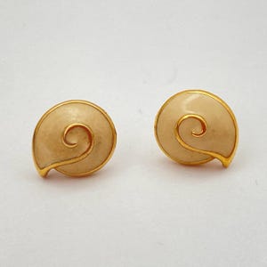 May include: A pair of gold tone stud earrings with a white enamel swirl design.