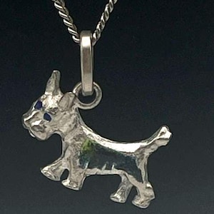 May include: Silver-toned pendant necklace featuring a stylized dog charm. The dog charm has blue accents for the eyes and is suspended from a twisted silver chain. The pendant is approximately 1 inch in length.