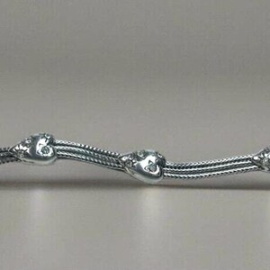 Peut inclure: Un bracelet en argent avec un design de cha&icirc;ne et des breloques en forme de c&oelig;ur. Chaque breloque en forme de c&oelig;ur a de petites pierres claires.