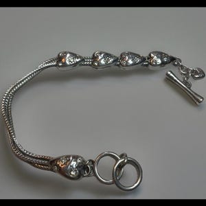 Peut inclure: Un bracelet en argent avec un design de cha&icirc;ne et cinq breloques en forme de c&oelig;ur. Chaque breloque est d&eacute;cor&eacute;e de petits strass transparents. Le bracelet a un fermoir &agrave; glissi&egrave;re.