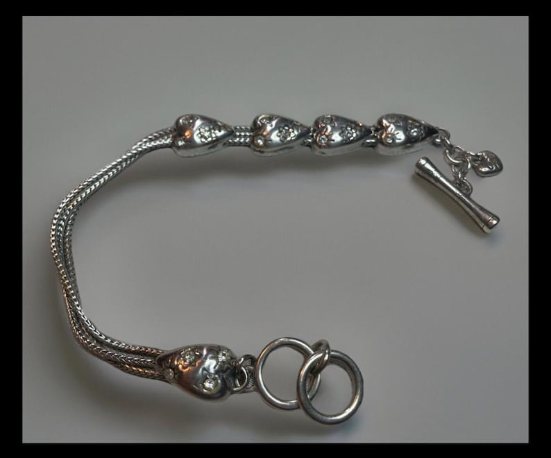 Peut inclure: Un bracelet en argent avec un design de cha&icirc;ne et cinq breloques en forme de c&oelig;ur. Chaque breloque est d&eacute;cor&eacute;e de petits strass transparents. Le bracelet a un fermoir &agrave; glissi&egrave;re.