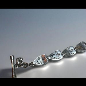 Peut inclure: Bracelet en argent avec un fermoir en forme de c&oelig;ur et une rang&eacute;e de breloques en forme de c&oelig;ur en argent. Chaque breloque en forme de c&oelig;ur pr&eacute;sente un motif floral.