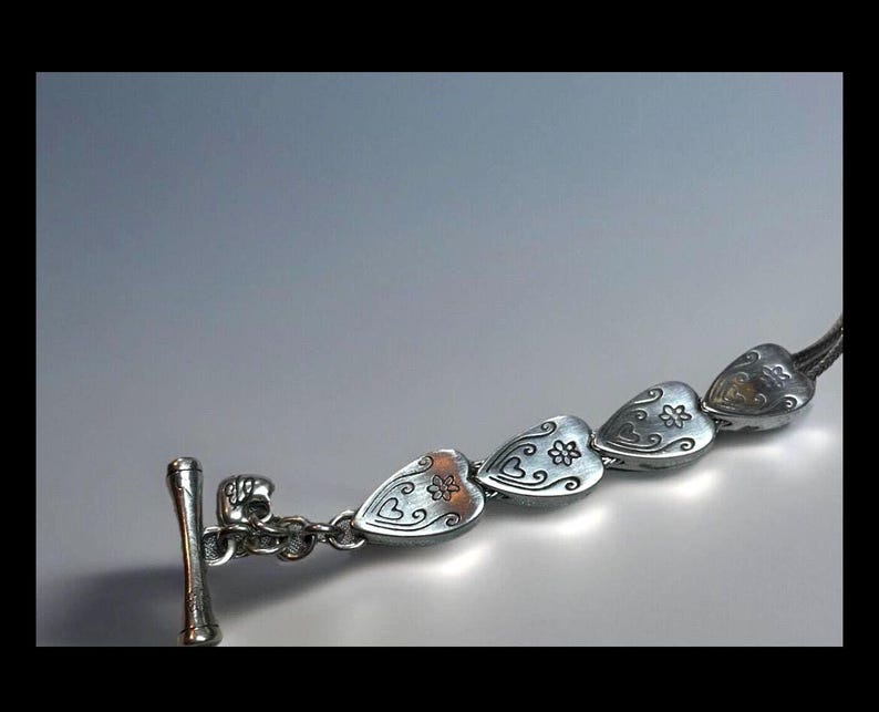 Peut inclure: Bracelet en argent avec un fermoir en forme de c&oelig;ur et une rang&eacute;e de breloques en forme de c&oelig;ur en argent. Chaque breloque en forme de c&oelig;ur pr&eacute;sente un motif floral.