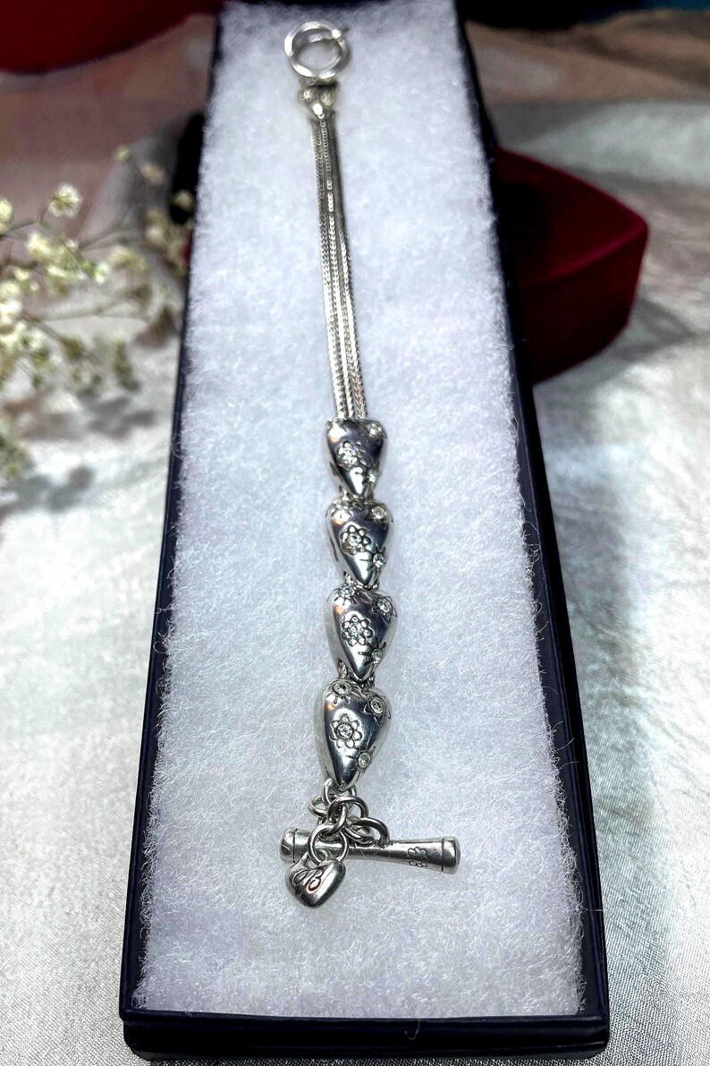 Peut inclure: Un bracelet en argent avec un motif de charme en forme de c&oelig;ur. Le bracelet a un fermoir &agrave; bascule et est compos&eacute; de plusieurs brins de cha&icirc;ne.