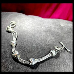 Peut inclure: Bracelet en argent avec un design de cha&icirc;ne &agrave; maillons et quatre breloques en forme de c&oelig;ur. Chaque breloque est d&eacute;cor&eacute;e de petites pierres claires.