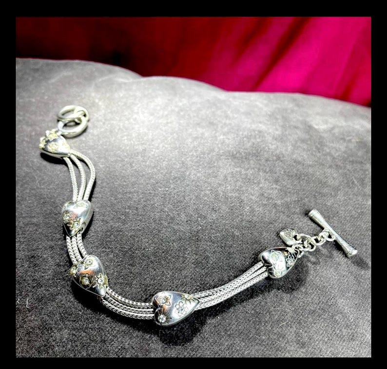 Peut inclure: Bracelet en argent avec un design de cha&icirc;ne &agrave; maillons et quatre breloques en forme de c&oelig;ur. Chaque breloque est d&eacute;cor&eacute;e de petites pierres claires.