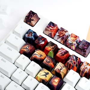 May include: A white mechanical keyboard with custom keycaps featuring colorful fantasy art. The keycaps are arranged in rows, with the white keys of the keyboard providing a contrasting background. The keycaps have various designs and colors.