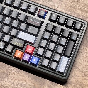 May include: A close-up shot of a mechanical keyboard with black keys and a dark grey frame. The keyboard has colourful accent keys in orange, red, purple, and blue. Some keys have text like "HELLO WORLD" and "BACKSPACE".