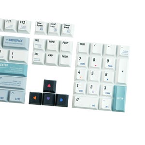 May include: A collection of white and black keyboard keys. The white keys have black lettering, including function keys, number pad, and navigation keys. Four black keys with colored arrow symbols are also visible.