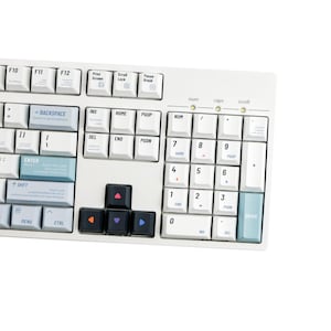 May include: A white mechanical keyboard with various keycaps. The keyboard features a standard layout with function keys, a number pad, and arrow keys. The keycaps are a mix of white, black, and colorful accent keys.