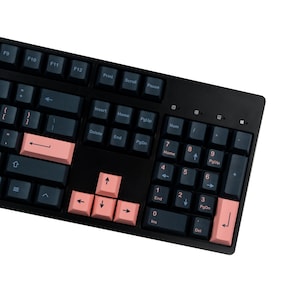 Może przedstawiać: Czarna klawiatura mechaniczna z ciemnoniebieskimi nakładkami na klawisze i łososiowymi klawiszami akcentującymi. Klawiatura ma standardowy układ z klawiszami funkcyjnymi, klawiaturą numeryczną i klawiszami strzałek. Klawisze są wyraźnie oznaczone białymi literami.