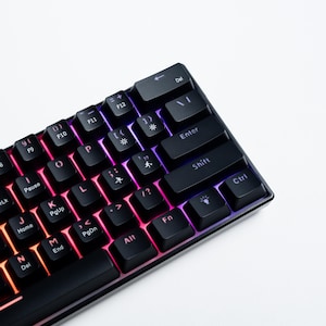 May include: A compact black mechanical keyboard featuring backlit keys with a vibrant red, orange, and purple gradient light effect. The keys display standard alphanumeric characters along with function labels like Enter, Shift, Ctrl, Alt, and Fn.
