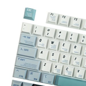 May include: Close-up of a computer keyboard with white and light blue keys. The keys have black lettering and symbols. Function keys and special keys like ESC, TAB, SHIFT, and CTRL are visible. The keyboard is designed for coding.