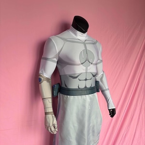 May include: A white and grey superhero costume on a mannequin. The costume has a high collar, long sleeves, and a detailed design on the chest and abdomen. A grey belt and white skirt complete the outfit.