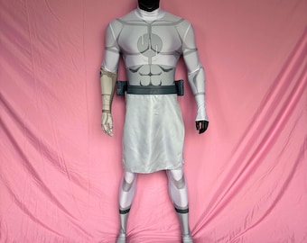 Puede incluir: Un disfraz de cuerpo completo en un maniquí. El disfraz es principalmente blanco con acentos grises, con un cuello alto, mangas largas y una prenda inferior tipo falda. El diseño incluye musculatura simulada y un cinturón con bolsillos. El maniquí tiene una cabeza negra.