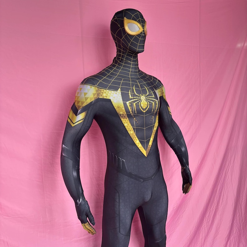 以下が含まれることがあります： 黒と金の スパイダーマンのコスチューム。全身タイツは胸にクモのエンブレム、肩、マスク、手袋に金のディテールが施されています。マスクには黄色のレンズが付いています。