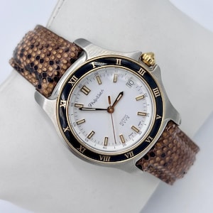 Op de afbeelding: Een zilverkleurig Philip Watch polshorloge met een witte wijzerplaat, zwarte lunette en gouden accenten. Het horloge heeft een bruine band met slangenpatroon. De wijzerplaat toont Romeinse cijfers en de tekst "HIPPOS MATE".
