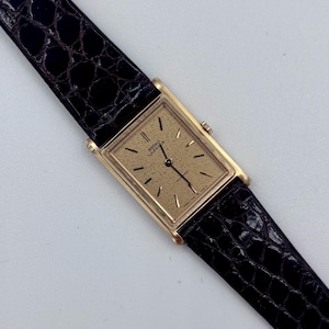 Pode incluir: Um relógio Seiko Lassale Quartz retangular dourado com mostrador dourado texturizado e pulseira de couro preta. O relógio tem um design clássico com caixa dourada e pulseira de couro preta, adequado para ocasiões formais.