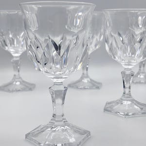 Op de afbeelding: Een set heldere glazen kelken met een gefacetteerd ruitpatroon op de kom, een veelzijdige steel en een zeshoekige voet. Het glaswerk is transparant met reflecterende oppervlakken en toont een geometrisch ontwerp door de gehele structuur.