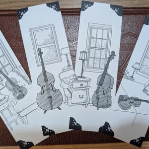 May include: A set of four rectangular paper bookmarks featuring black and white line art illustrations. Each bookmark depicts a different musical instrument, including a cello and a violin, set within a room with a window, lamp, and furniture.