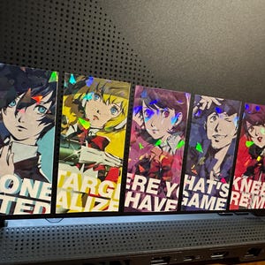 May include: Six holographic stickers featuring anime characters with text that reads "Done Stepped", "Targetalize", "Here You Have", "That's Game", "Knee Remind", and "On to Next".
