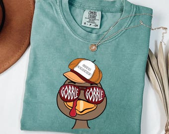 May include: A teal blue t-shirt with a cartoon turkey wearing sunglasses and a hat that says "Chief Turkey" printed on the front.