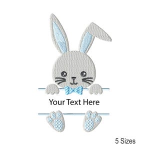 May include: An embroidered design of a grey bunny with light blue accents. The bunny has a bow tie and is holding a banner that says "Your Text Here". The design also includes two bunny feet and the text "5 Sizes".