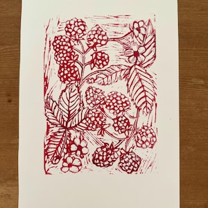 Può includere: Una stampa linoleografica rossa su carta bianca con un design botanico di lamponi, foglie e fiori. La stampa ha un'estetica artigianale, con texture e dettagli visibili. Le bacche e il fogliame sono finemente resi.