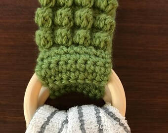 May include: A green crocheted towel ring with a wooden ring. The towel ring is made with a bobble stitch and the wooden ring is unfinished.
