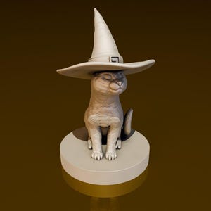 Puede incluir: Una figurita de cerámica blanca de un gato con un sombrero de bruja puntiagudo. El gato está sentado sobre una base redonda.