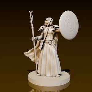 Puede incluir: Una figura en miniatura pintada de blanco de una maga sosteniendo un bastón y un escudo. La maga lleva una túnica larga y tiene el pelo largo.