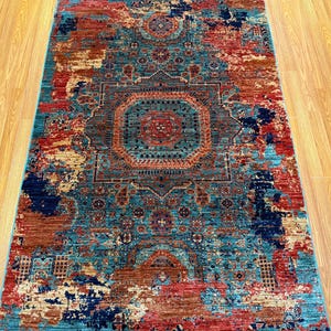 K&ouml;nnte beinhalten: Ein rechteckiger Teppich mit einem aufwendigen, verwitterten Design. Der Teppich zeigt ein zentrales Medaillon und einen Rand in T&uuml;rkis, Rot, Rost und Marineblau. Das Muster des Teppichs hat ein Vintage-Aussehen.