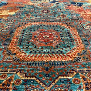 K&ouml;nnte beinhalten: Ein gro&szlig;er, rechteckiger Teppich mit einem aufwendigen, verwitterten Muster. Der Teppich hat ein zentrales Medaillon-Design in T&uuml;rkis, Orange und Marineblau. Die Gesamt&auml;sthetik ist eine Mischung aus traditionellen und modernen Stilen.