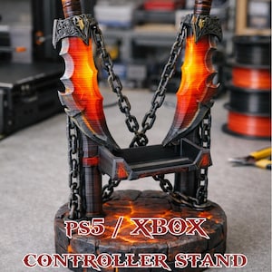 May include: A controller stand inspired by "God of War," shaped like two swords with fiery blades, linked by chains. The base is textured, with the text "PS5 / XBOX CONTROLLER STAND." The stand is designed to hold a controller.