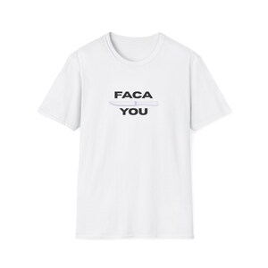 May include: White t-shirt with a crew neck and short sleeves. The shirt features the text "FACA YOU" in black block letters, with a light grey knife graphic between the words.