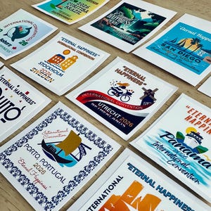 May include: A collection of rectangular stickers featuring various graphic designs for the 2026 Eternal Happiness International Convention. Each sticker displays a unique city name, including Milwaukee, Panama, Porto, Utrecht, Stockholm, San Diego, and Curitiba.