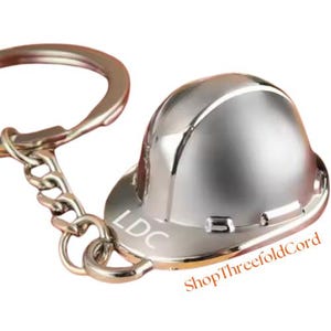 May include: Silver hard hat keychain with the letters LDC engraved on the side.