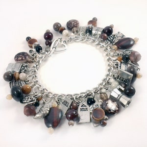 Puede incluir: Un brazalete de plata con una variedad de dijes con temática de café, incluyendo granos de café, tazas y palabras como "Java" y "Latte". El brazalete también presenta cuentas marrones y negras.