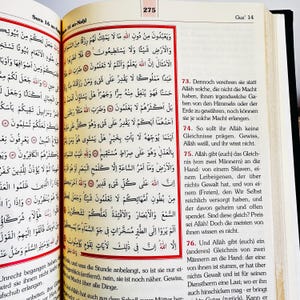 May include: An open book with Arabic text, featuring red and black accents. The pages are yellowed, and the book is open to a specific passage. The book is likely a religious text, possibly the Quran.