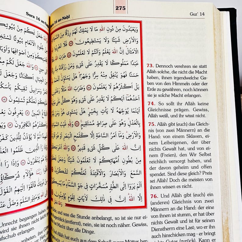 May include: An open book with Arabic text, featuring red and black accents. The pages are yellowed, and the book is open to a specific passage. The book is likely a religious text, possibly the Quran.